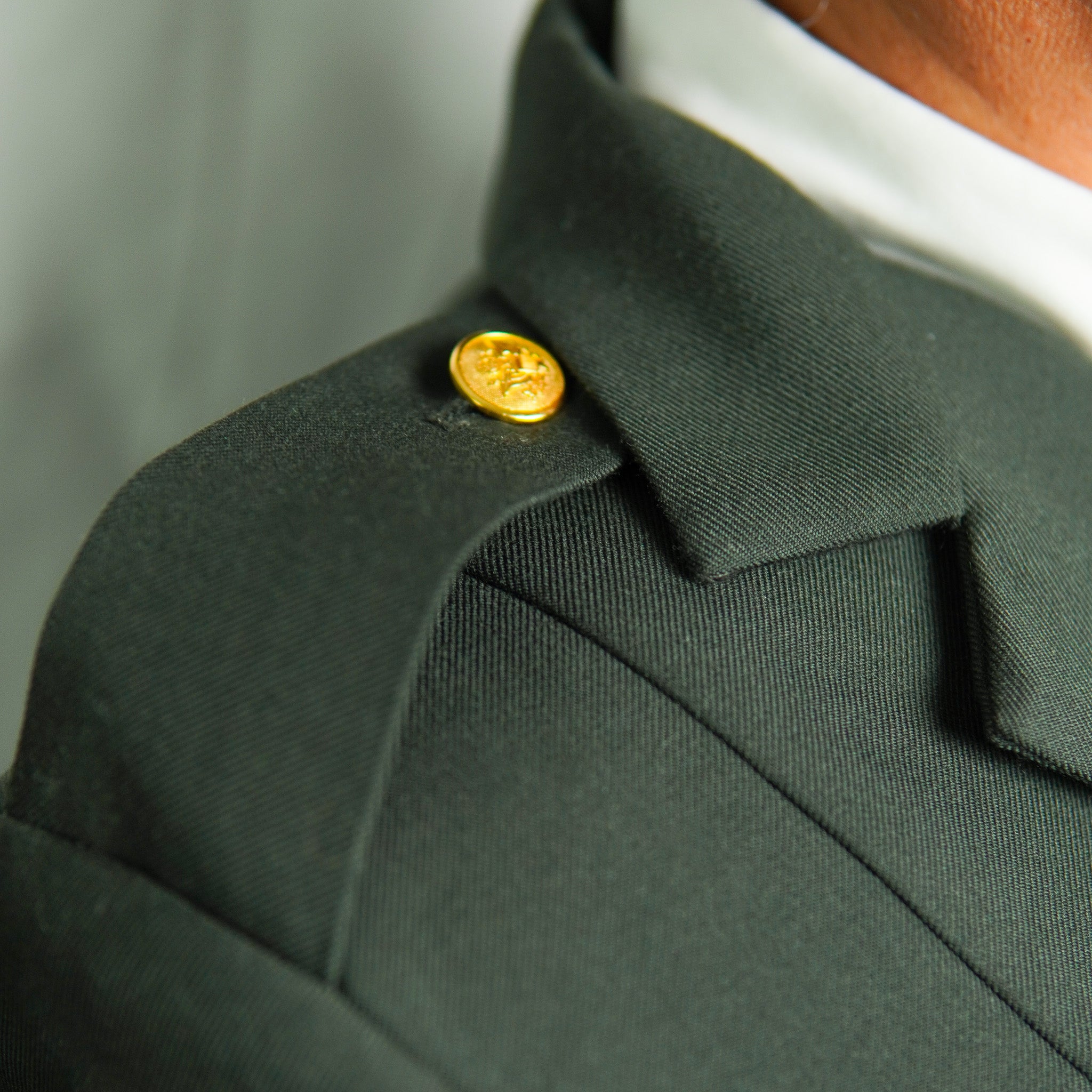 Close-up of a green jacket with a gold button on a blurred background