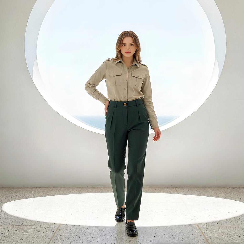 Woman wearing a beige shirt and green pants standing in a modern indoor setting with circular light fixtures.